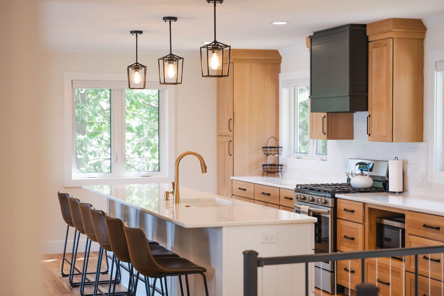 Modern kitchen with white quartz island, bar stools, pendant lights, wood cabinets, and gas range.
