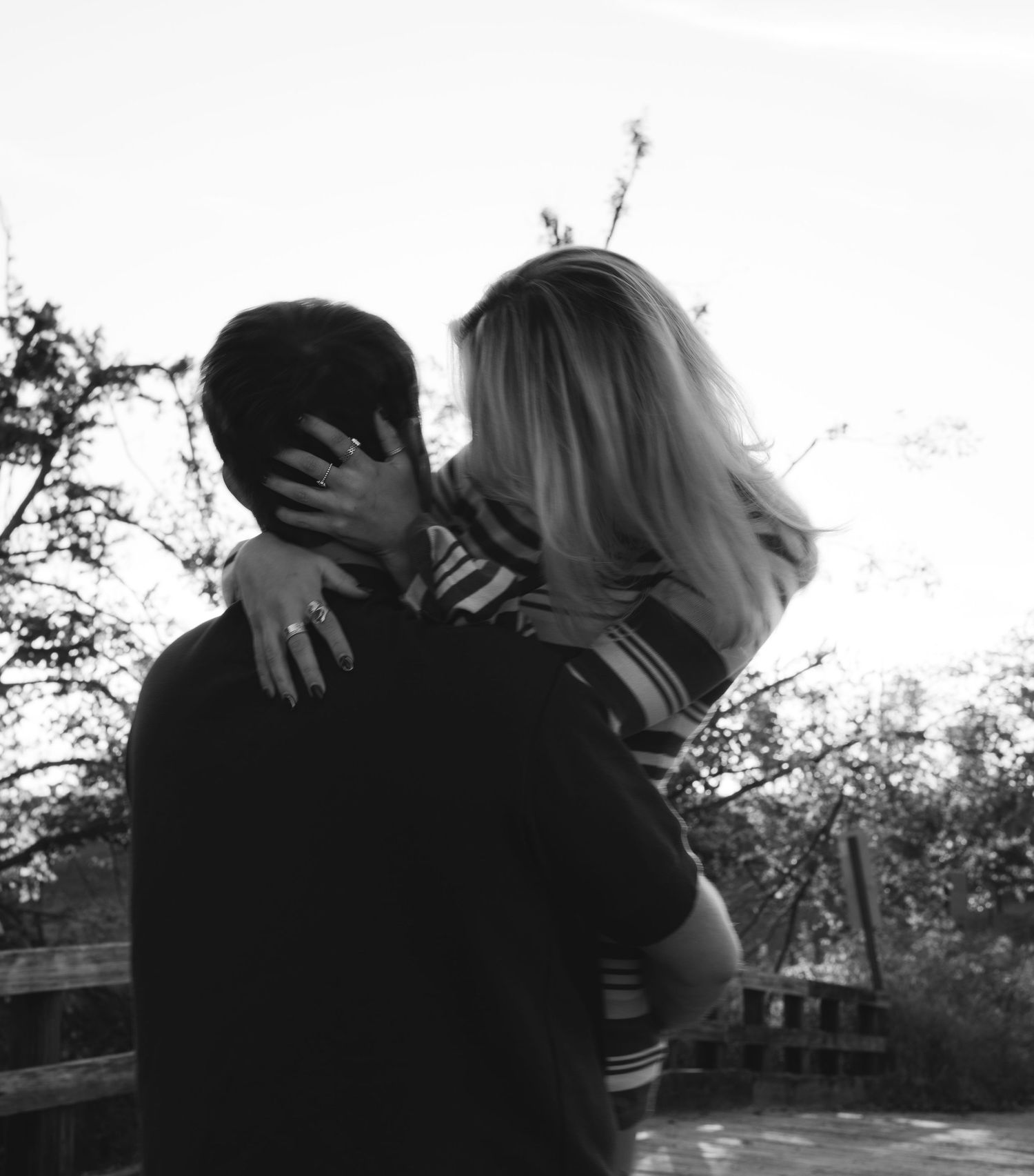 Black and white silhouette of a couple embracing tenderly outdoors with trees in background.