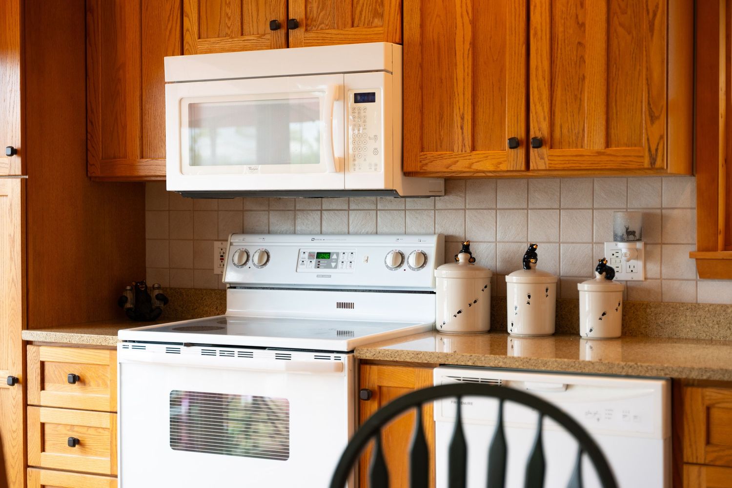 Classic kitchen with honey oak cabinets, white appliances, tile backsplash, and ceramic canister set.
