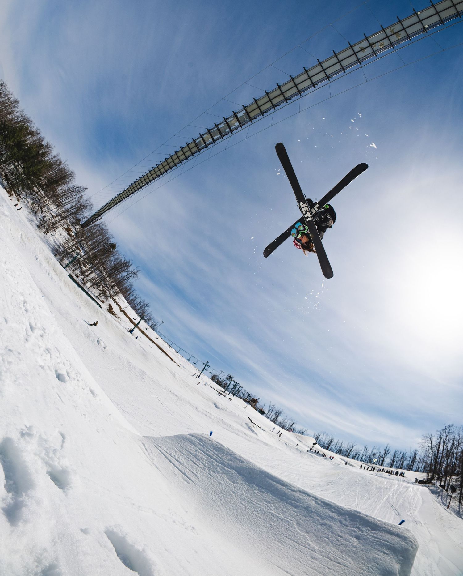 Skier performing an inverted aerial trick at a snow park under a bright blue sky.