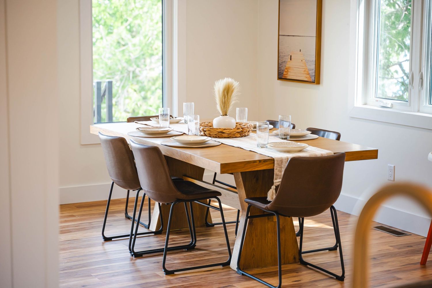 Modern dining room with wood table, brown chairs, hardwood floors, and natural light.