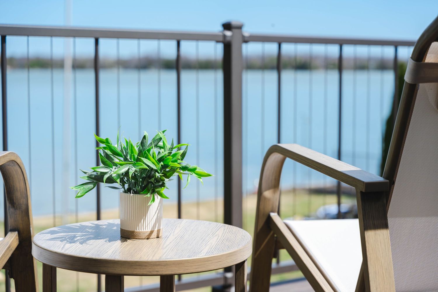 Waterfront balcony with chairs, small table, potted plant, and scenic water views.