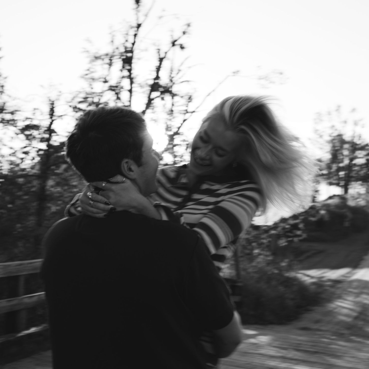 Black and white photo of a joyful couple embracing outdoors with trees in the background.