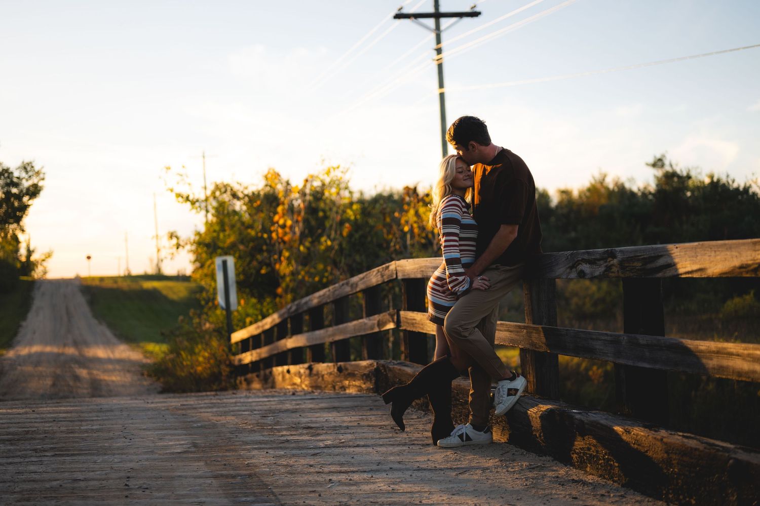 Romantic couple sharing a kiss on a rustic wooden bridge at golden hour sunset.