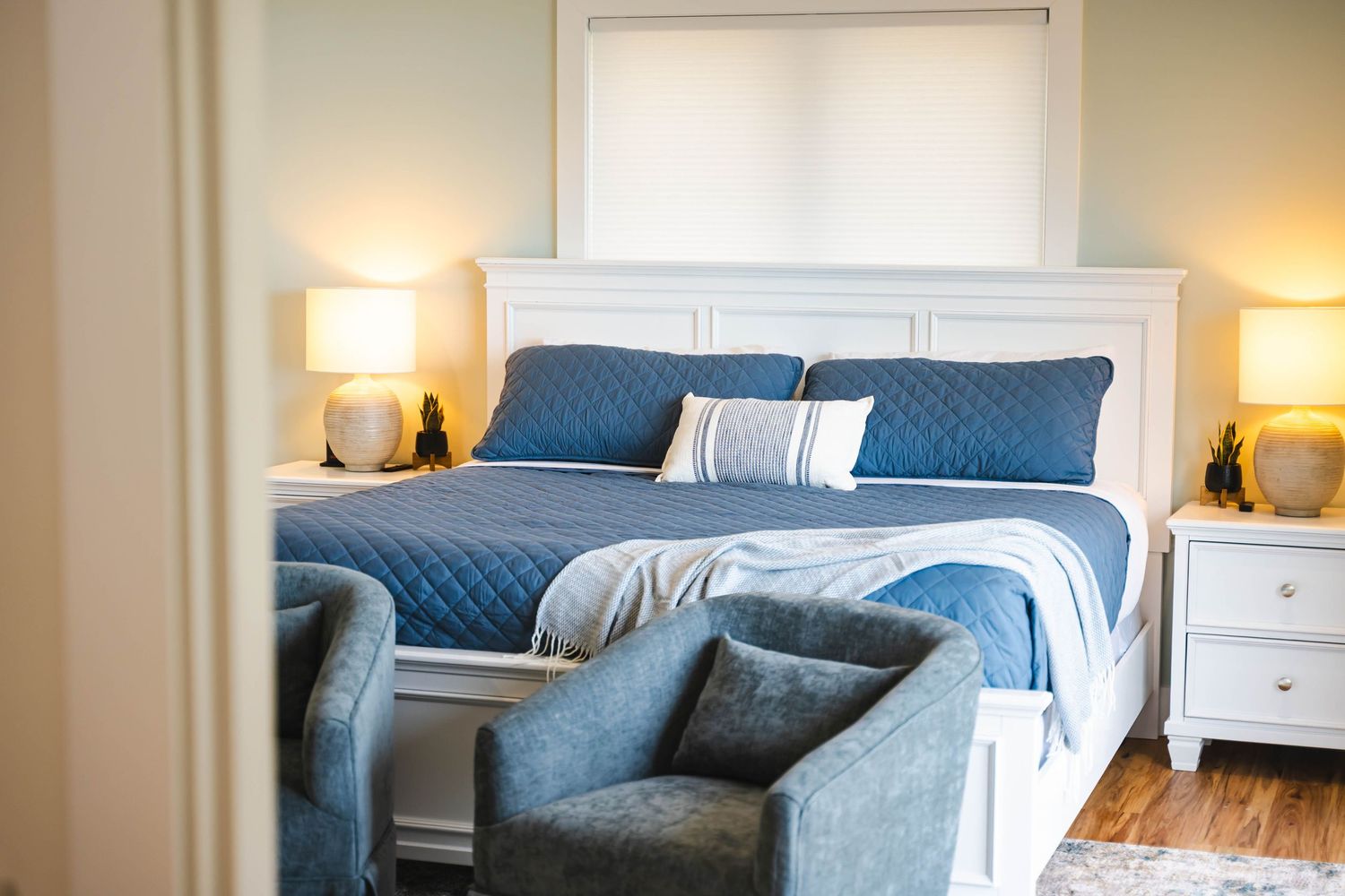 Elegant bedroom with white headboard, blue bedding, matching nightstands, and warm lighting.