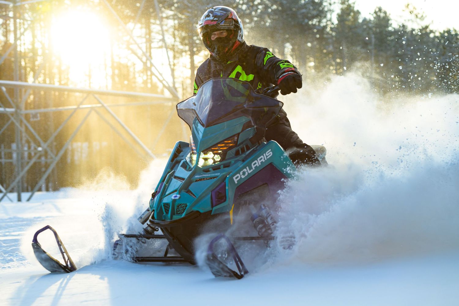 Rider on a teal Polaris snowmobile racing through fresh powder snow at sunset in winter.