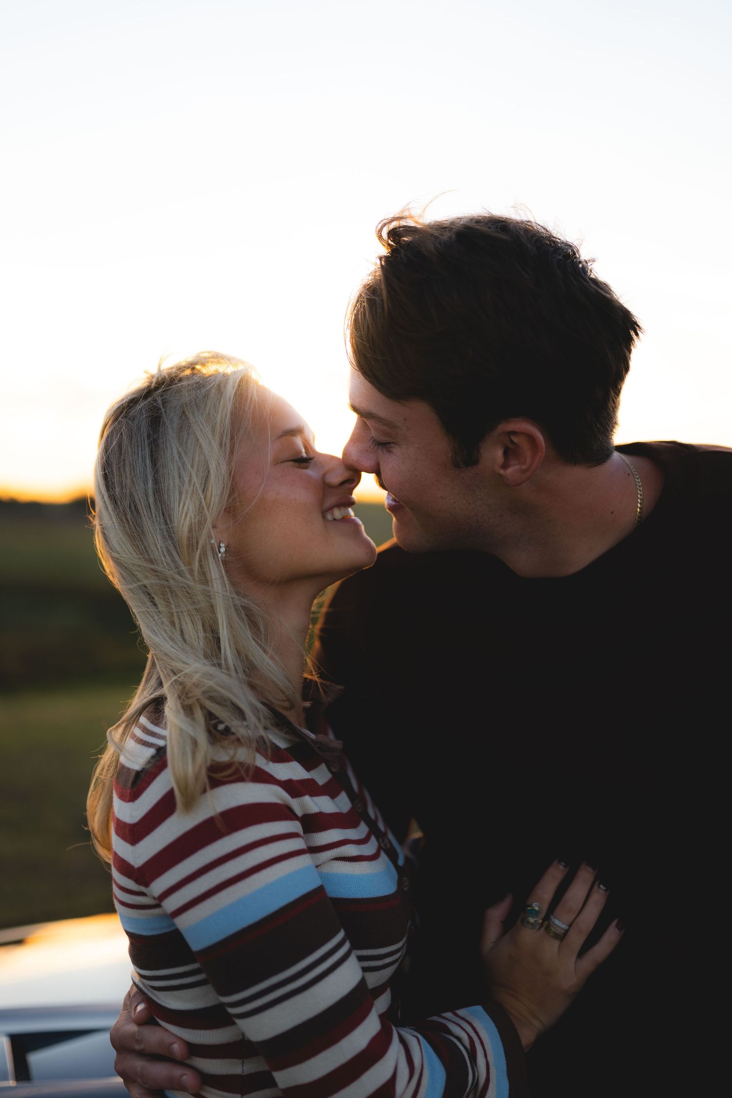 Couple sharing a romantic kiss outdoors with a glowing golden sunset in the background.