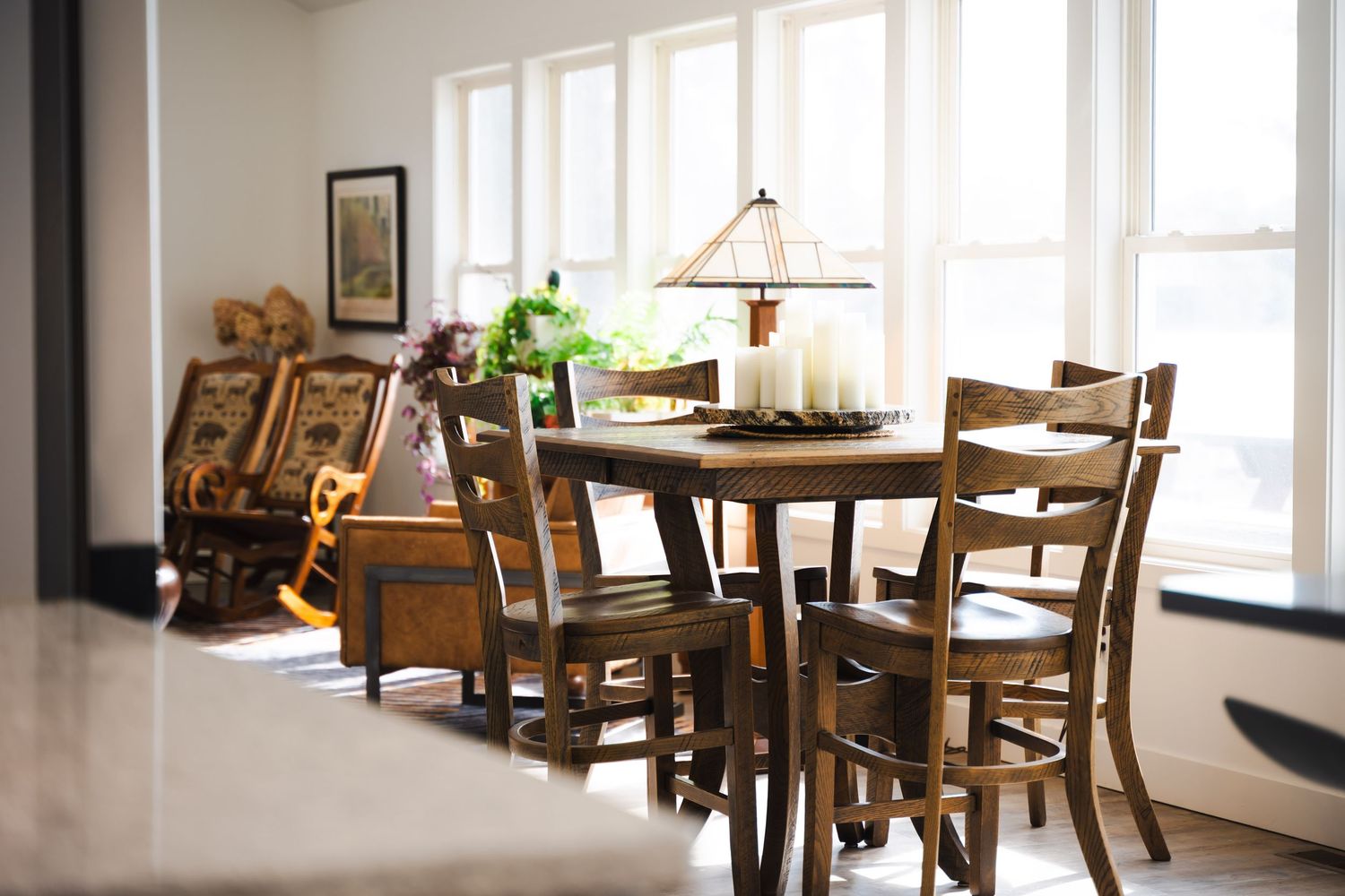 Rustic wooden dining table and chairs set in a bright room with large windows and decorative lamp centerpiece.