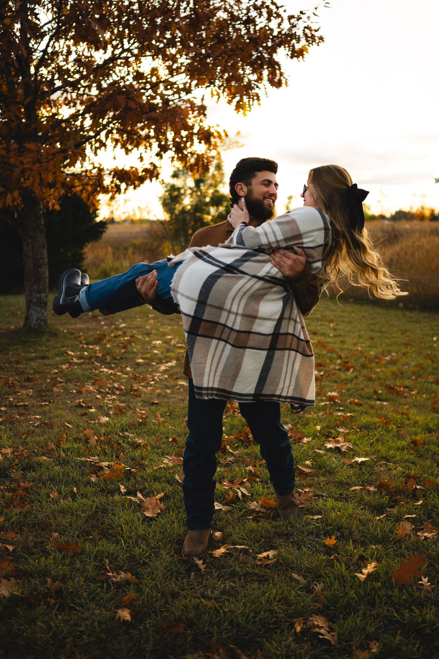 Man lifting and spinning his laughing partner in an autumn park with colorful fall leaves.