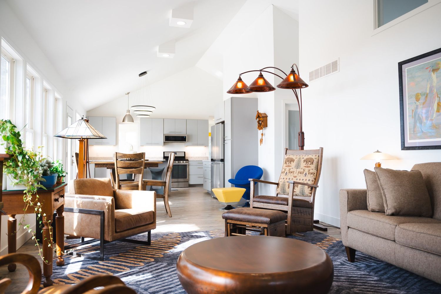 Bright open-concept living room with vaulted ceilings, mixed furniture, and view into modern white kitchen.