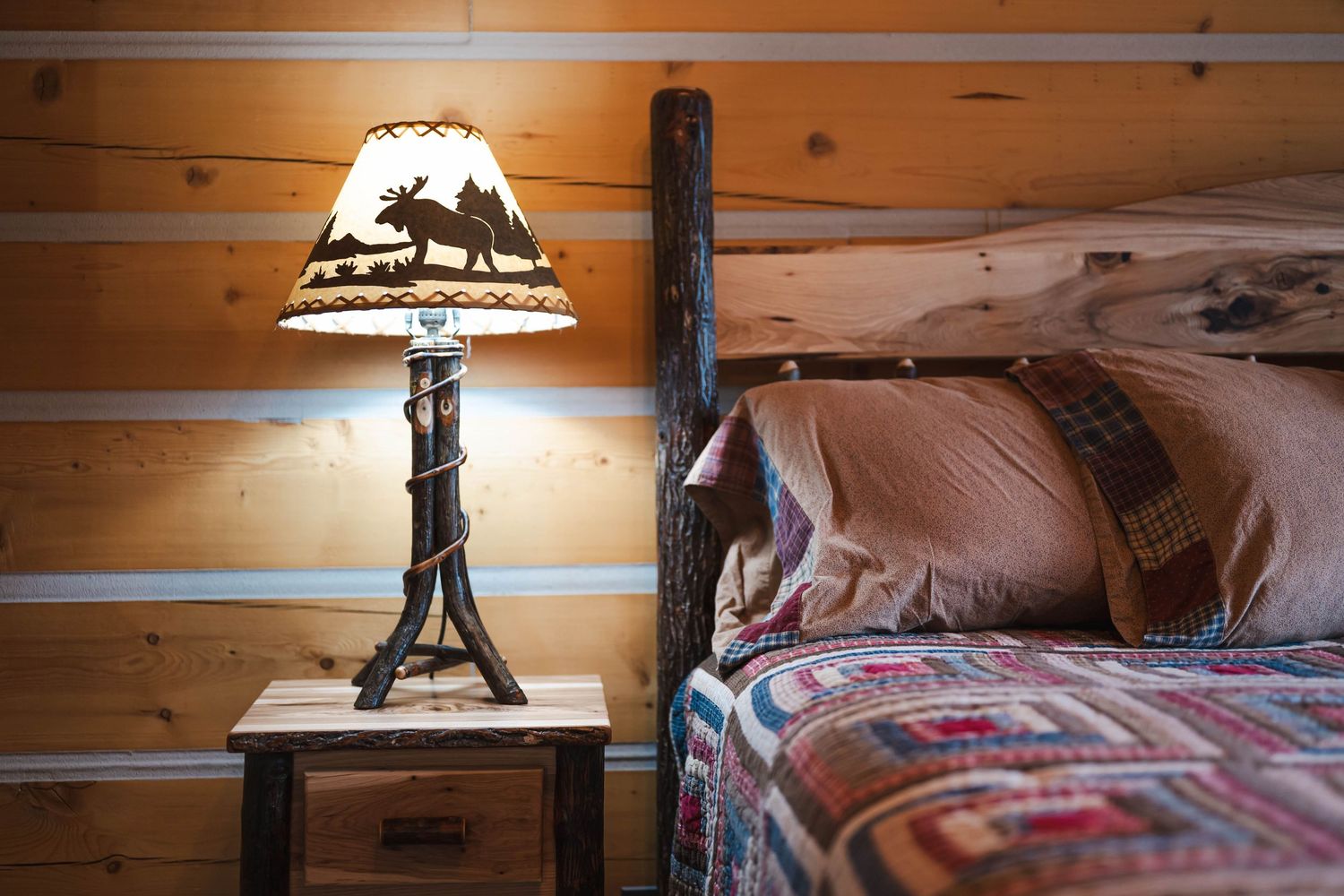 Cozy log cabin bedroom with rustic moose lamp and colorful patchwork quilt.