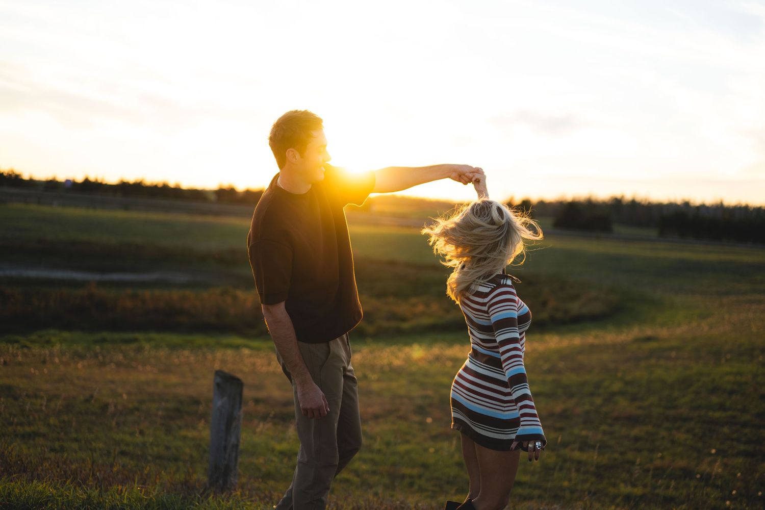 Couple dancing in a golden sunset field, man spinning woman in a striped dress.