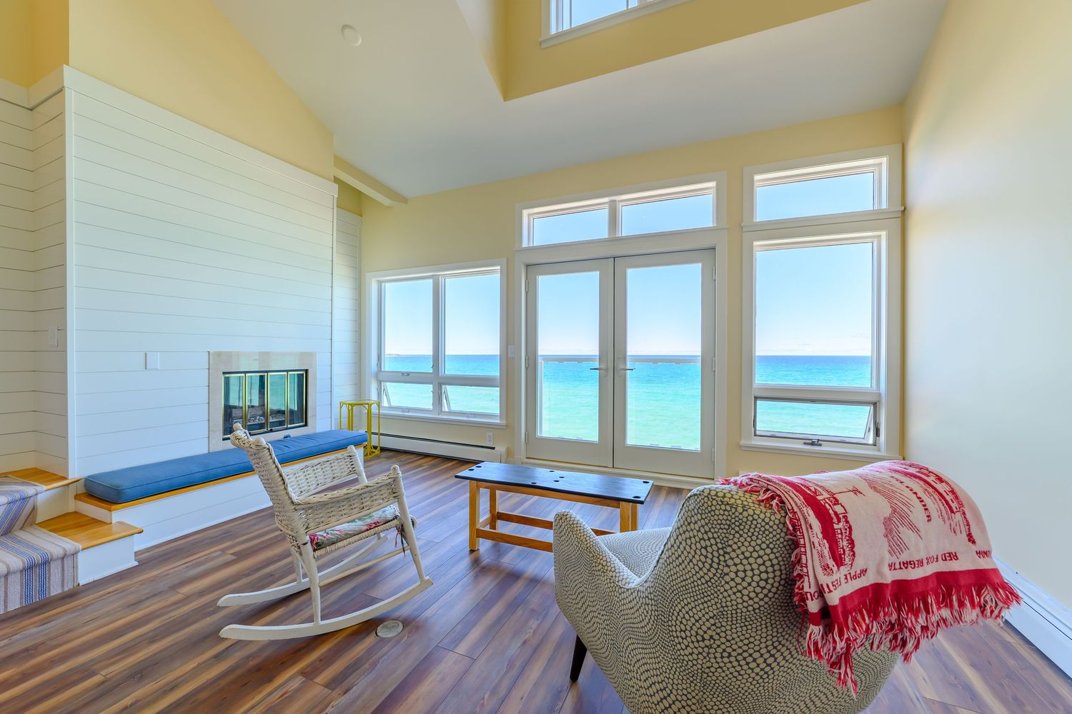 Bright beachfront living room with rocking chairs and panoramic ocean views through large windows.