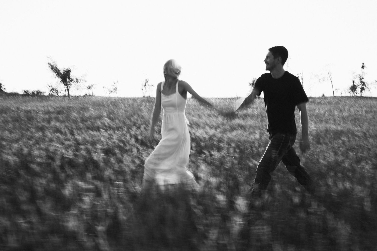 Black and white photo of a couple holding hands walking through a field.