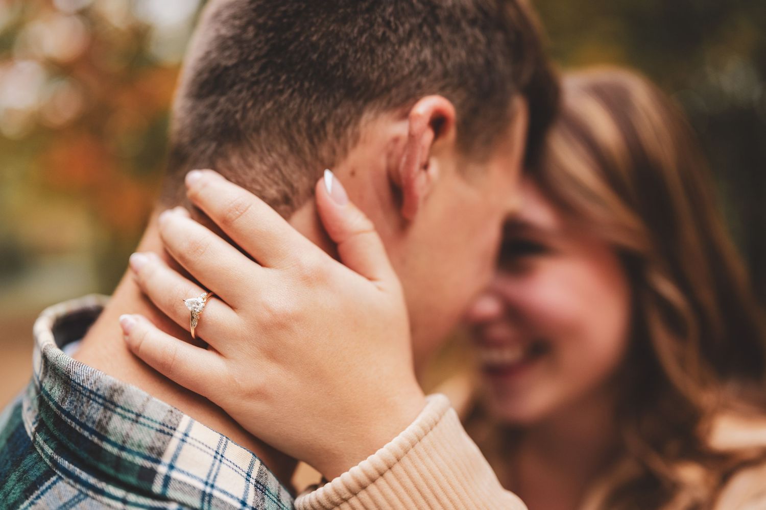 A close-up of a couple nearly kissing, with focus on the womans ring and hand cradling his head.