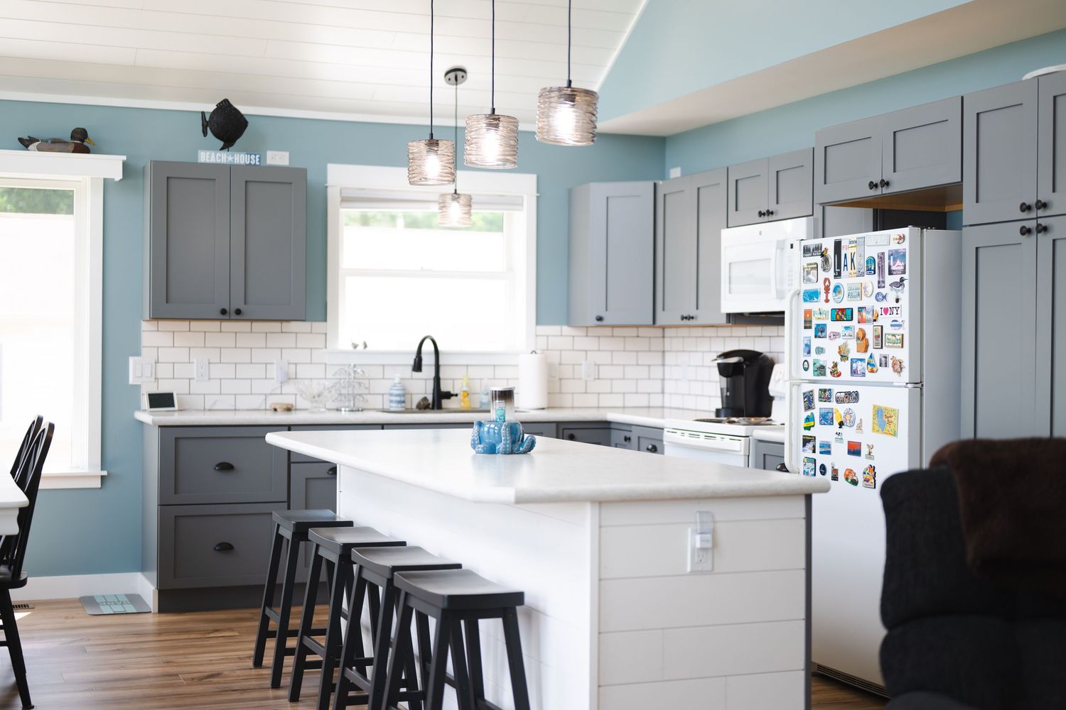 Modern kitchen with gray cabinets, white subway tile backsplash, island with bar stools, and blue walls.
