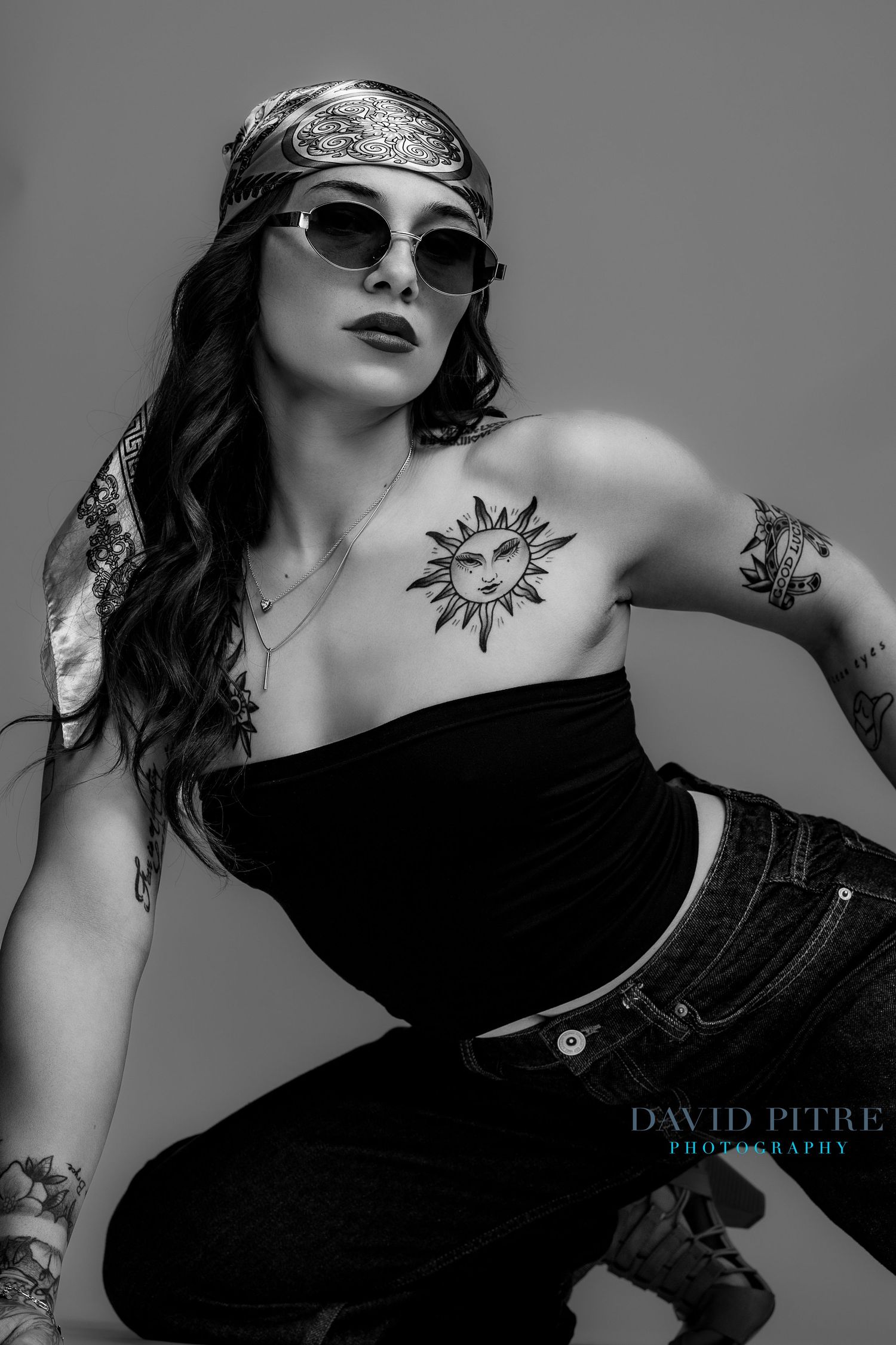 Artistic black and white fashion photo series showing model in black dress with sun tattoo and sunglasses striking poses.