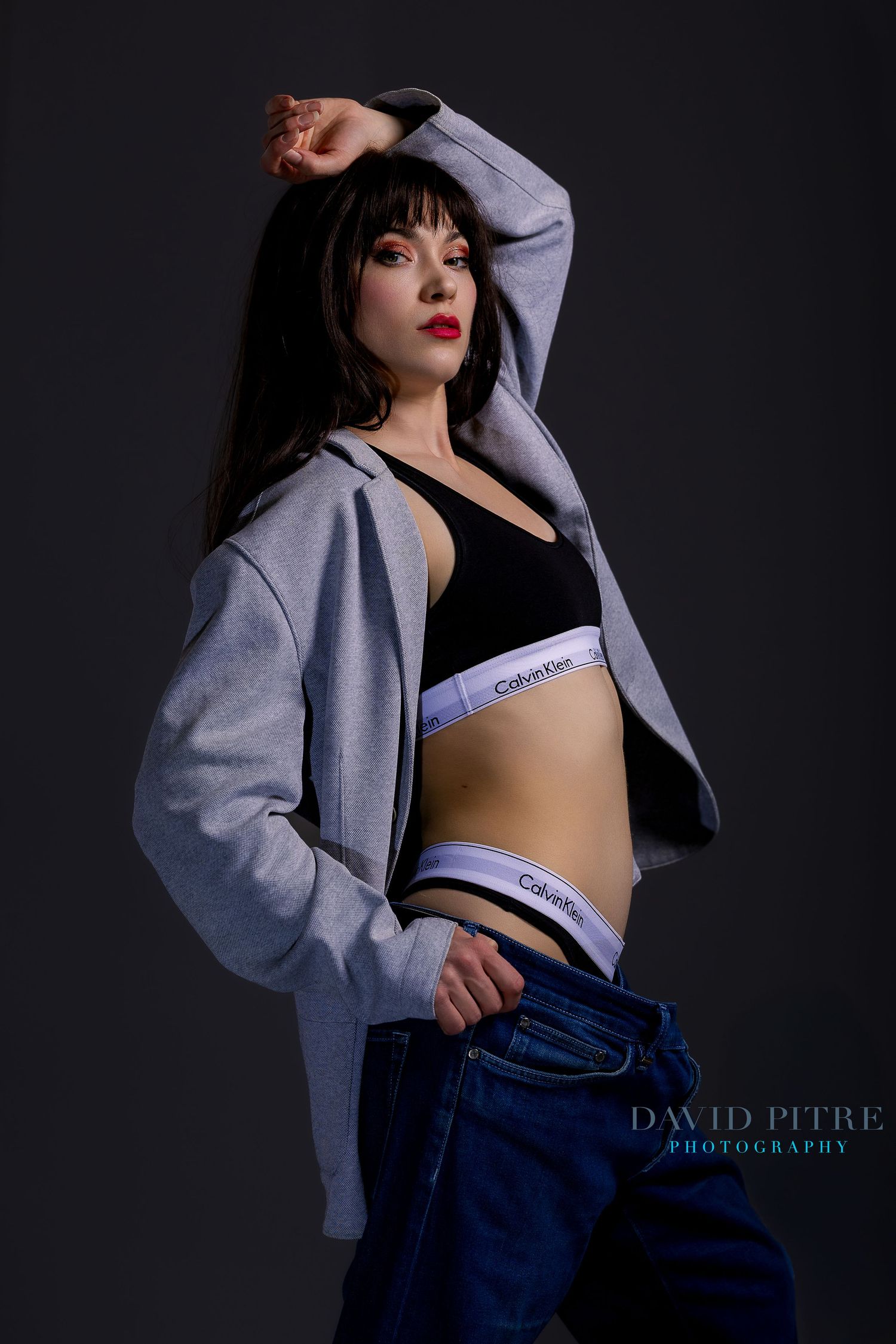 Fashion photo series showing model in Calvin Klein bra and jeans with grey oversized jacket against dark background.
