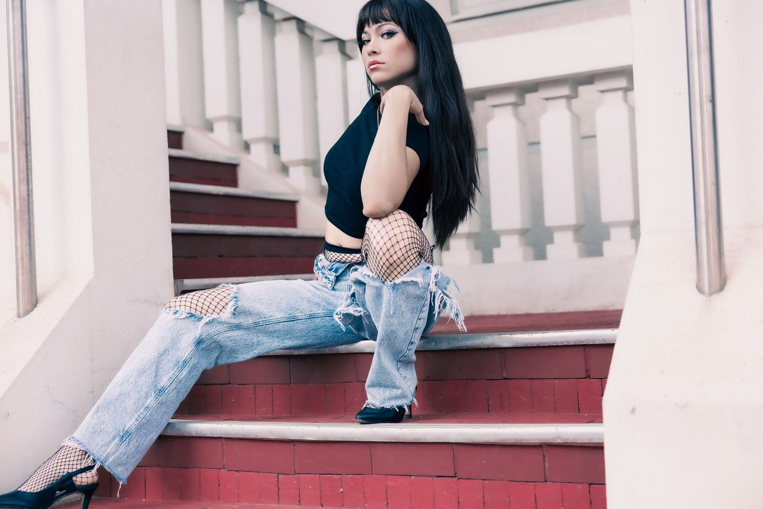 Woman in denim and white top sits elegantly on white marble stairs in a classic architectural setting.