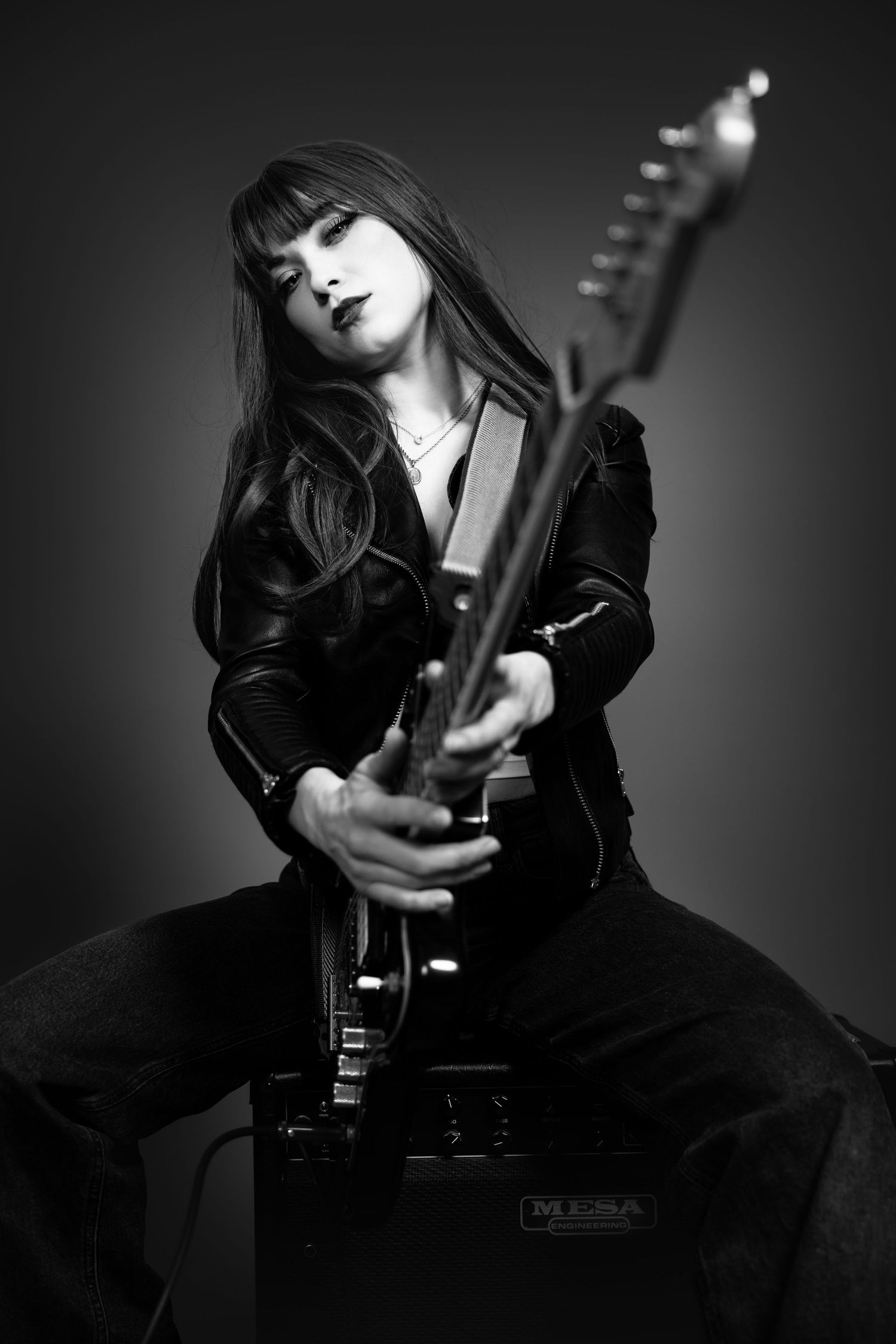 A dramatic black and white photo series showing someone in dark clothing posing with a guitar against a shadowy background.