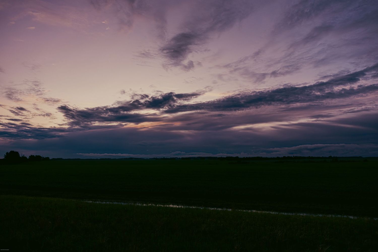 A dramatic purple and pink sunset sky stretches over a dark silhouetted landscape at dusk.