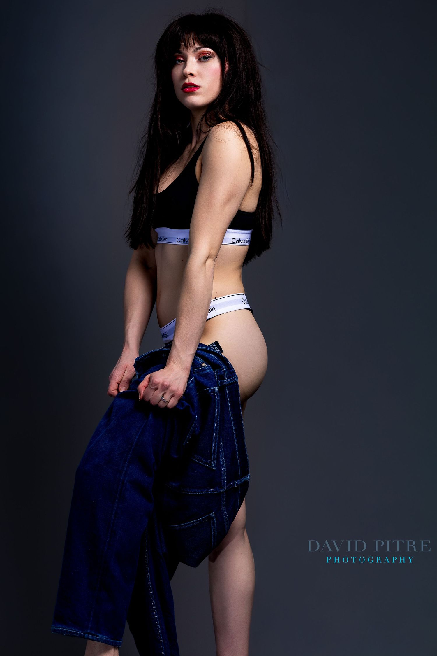 Artistic fashion series with denim and Calvin Klein sportswear against dramatic dark backdrop.