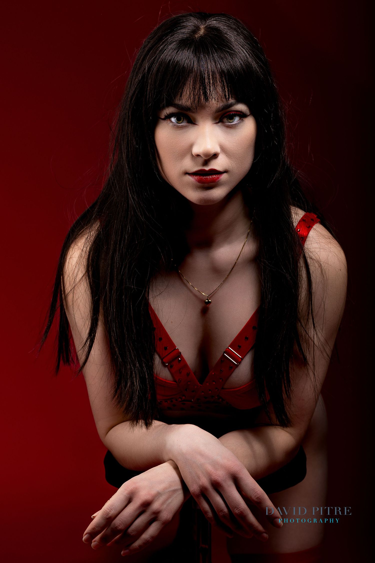 Portrait of someone in a red outfit against dark red background with dramatic studio lighting and striking makeup.