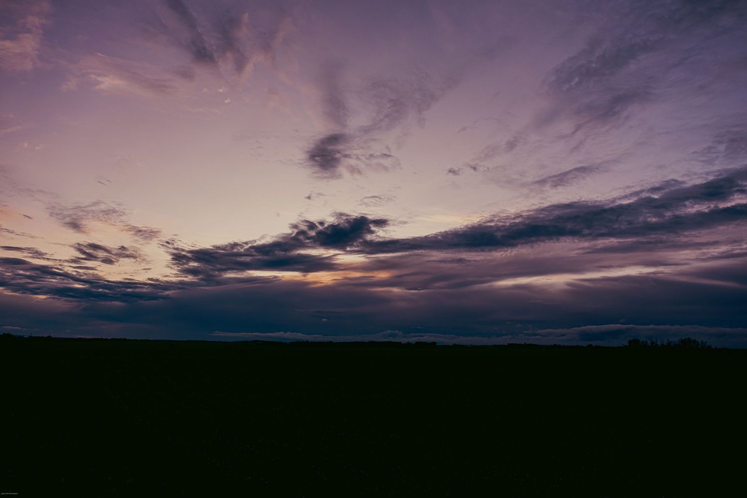 A panoramic series of dark silhouetted hills against a dramatic purple and pink sunset sky with scattered clouds.