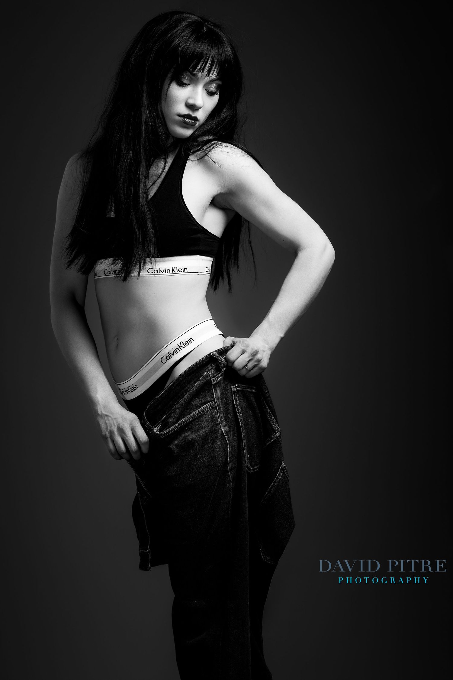 Dramatic monochrome portrait featuring model in Calvin Klein crop top and denim with moody lighting.