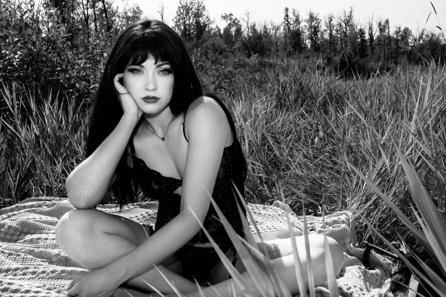 A black and white artistic photoshoot in a grassy outdoor setting with dramatic natural lighting and shadows.