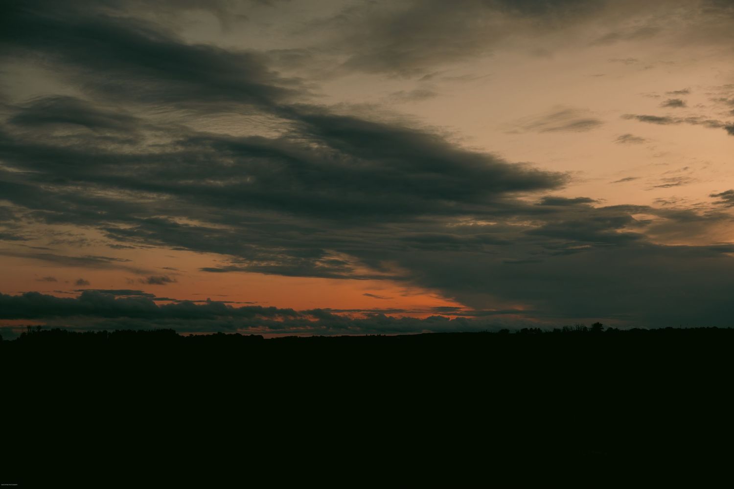 Dark silhouetted landscape against a moody sunset sky with dramatic orange clouds and deep shadows.