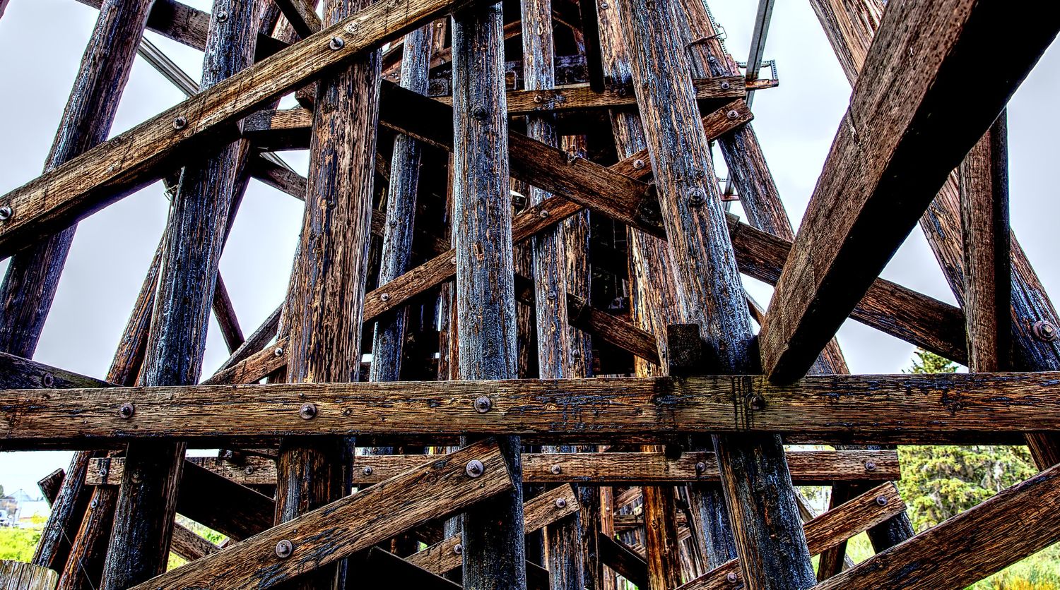Close-up view of rusty metal railroad bridge trusses and beams against a blue sky background.