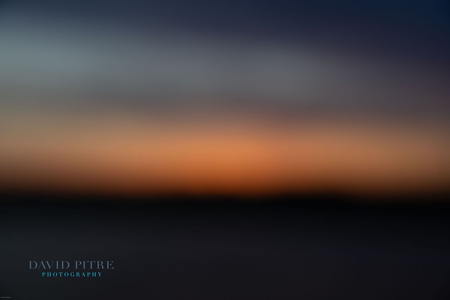 Abstract blurred landscape at sunset with dark silhouetted horizon and orange to blue gradient sky.