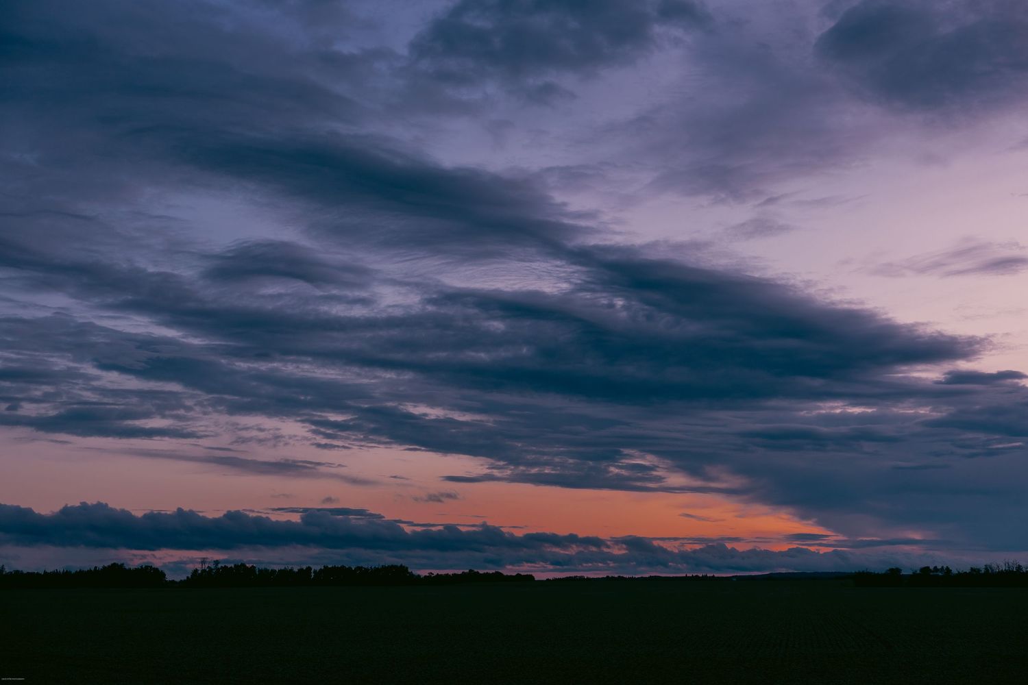 Dramatic dark clouds roll across a moody twilight sky with streaks of orange and purple on the horizon.