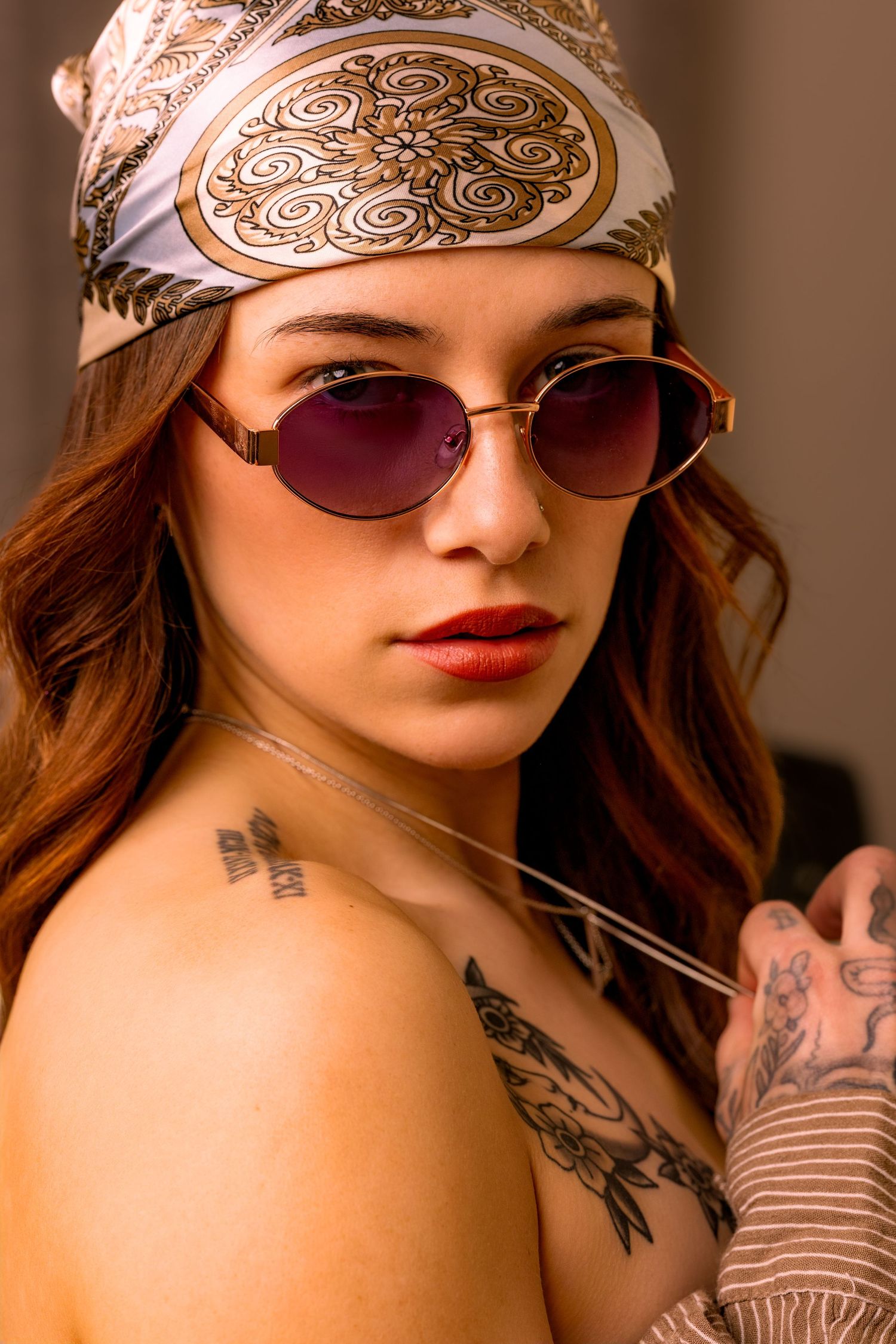 Portrait with patterned bandana, sunglasses and visible tattoos in warm lighting with vintage aesthetic.