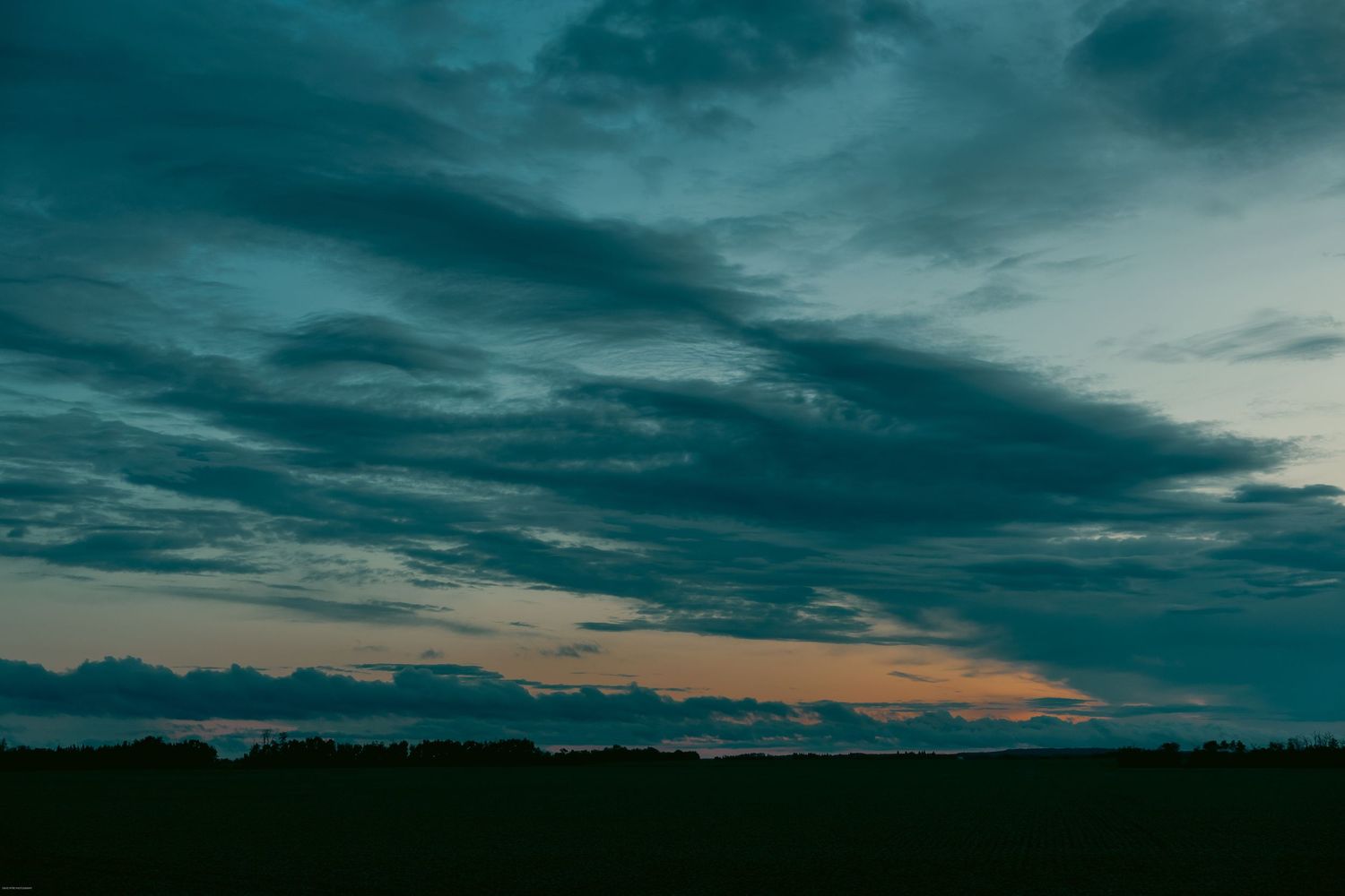 Stormy clouds form a dramatic pattern against a dusky sky with hints of orange sunset peeking through.