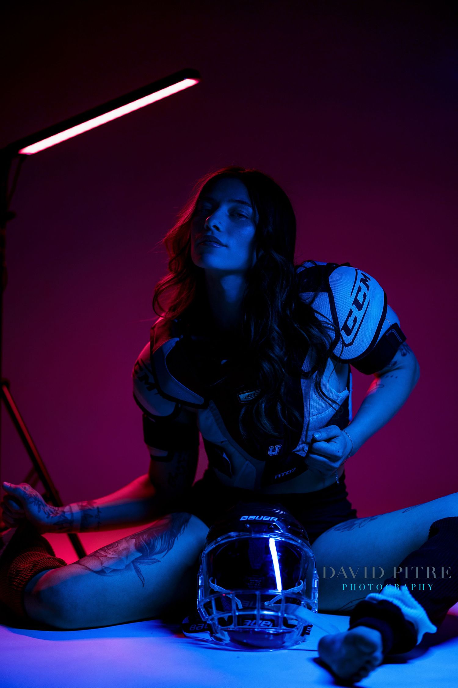 Low-key portrait with hockey equipment highlighted by dramatic purple and blue lighting effects.