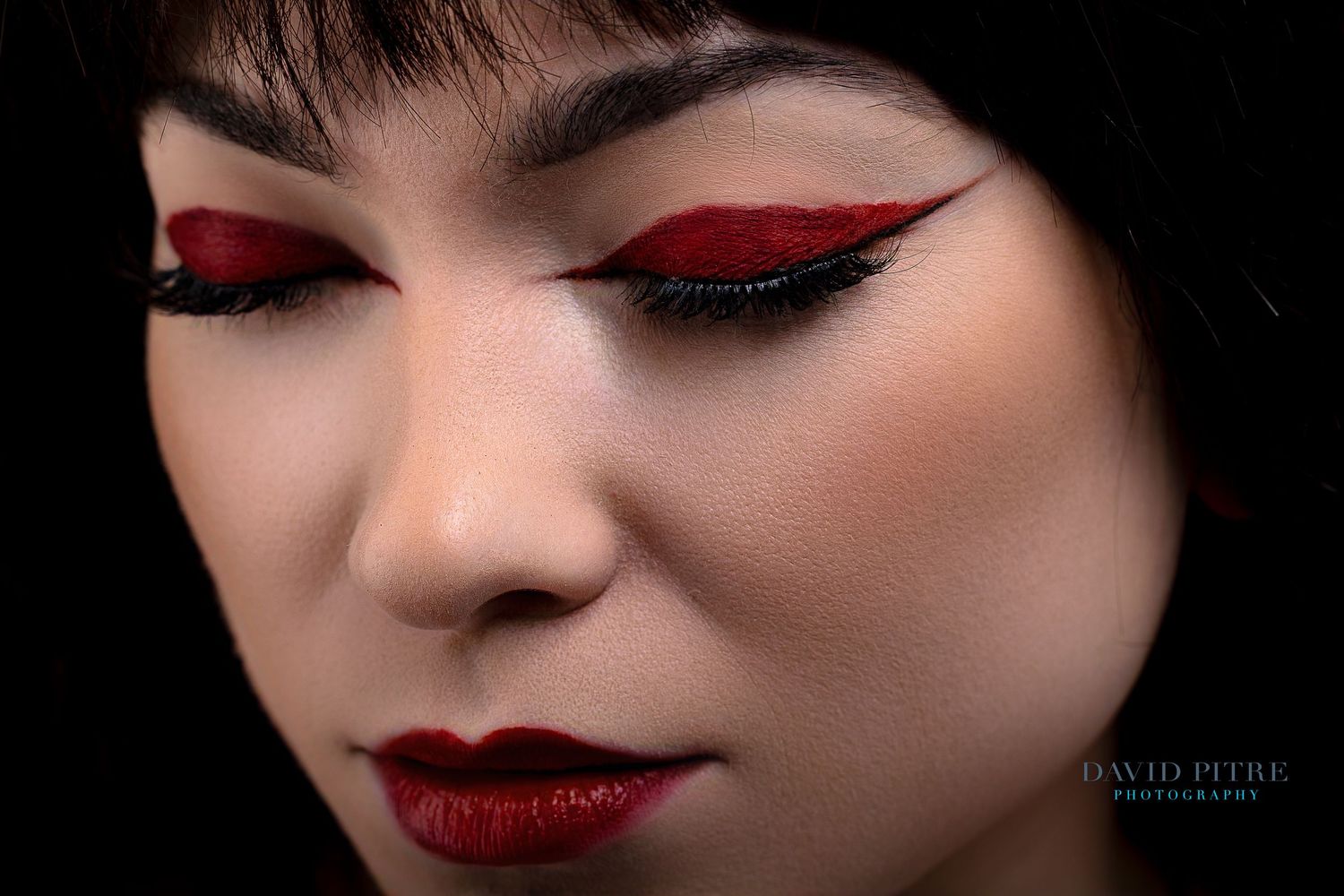 Close up beauty shot featuring dramatic red and black eye makeup with glitter and matching red lips.