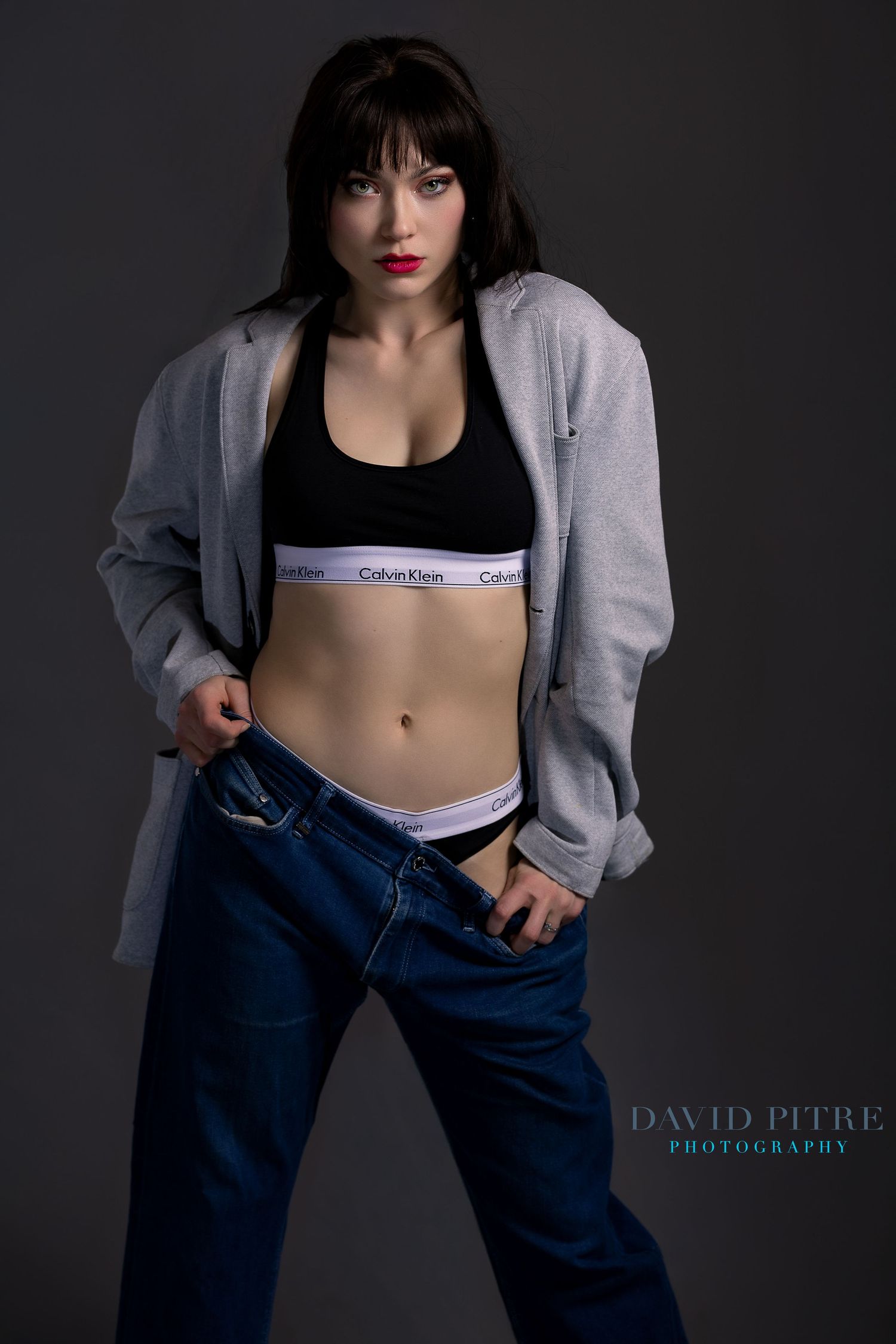 Black and white fashion photo showing a model in Calvin Klein top, jeans and grey cardigan against dark backdrop.