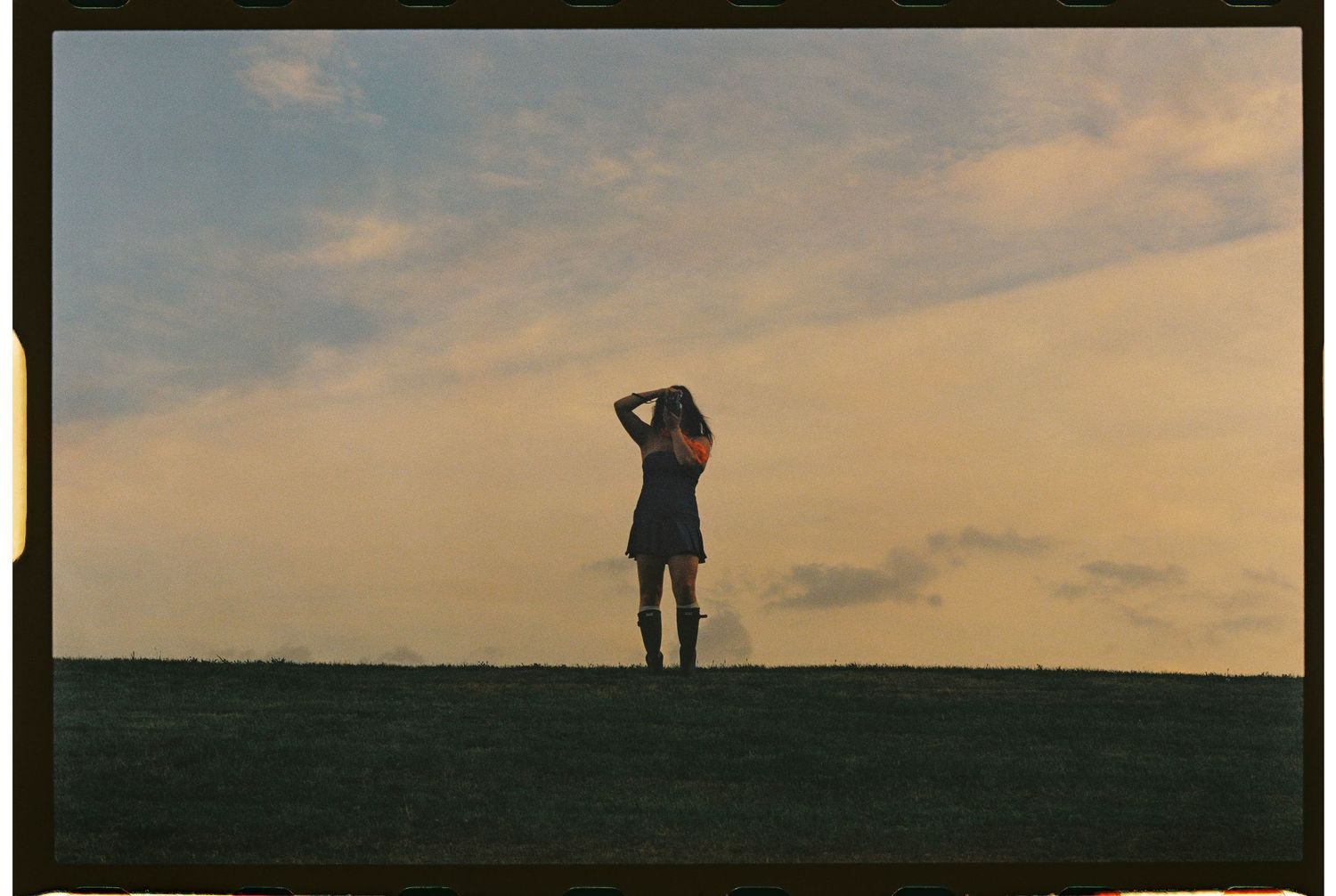 Silhouette of person standing on hill at golden sunset with dramatic cloudy sky.
