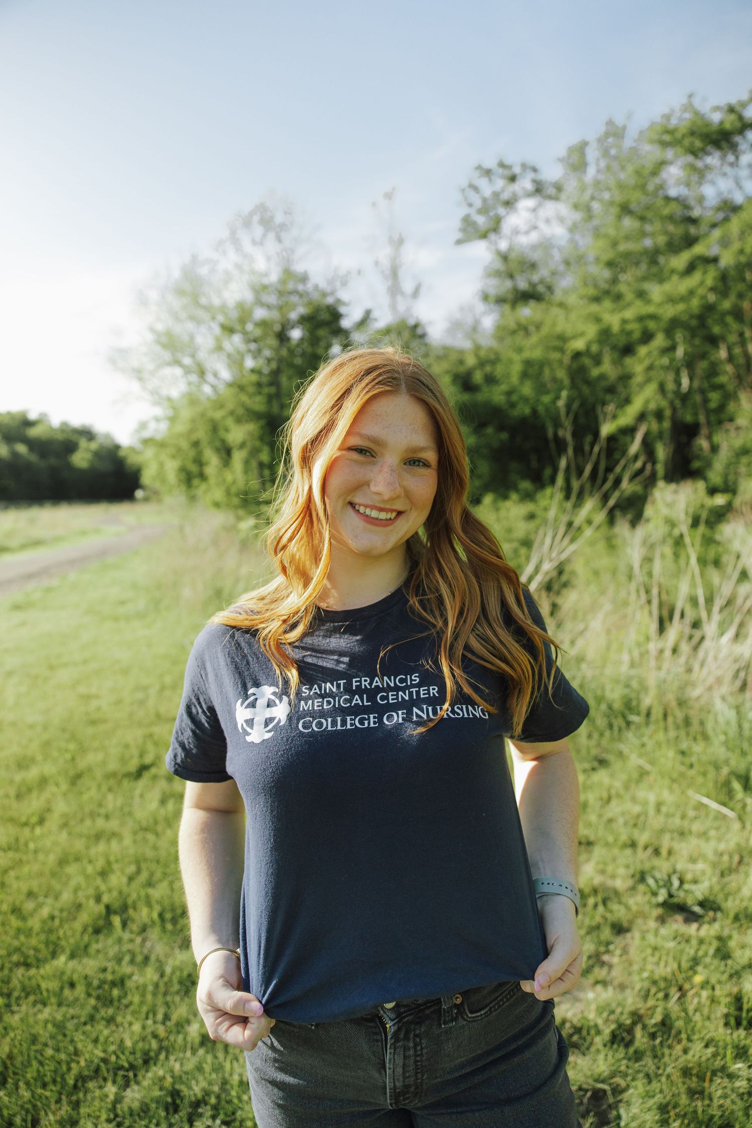 Young woman in Saint Francis Medical Center College of Nursing navy t-shirt smiling outdoors.
