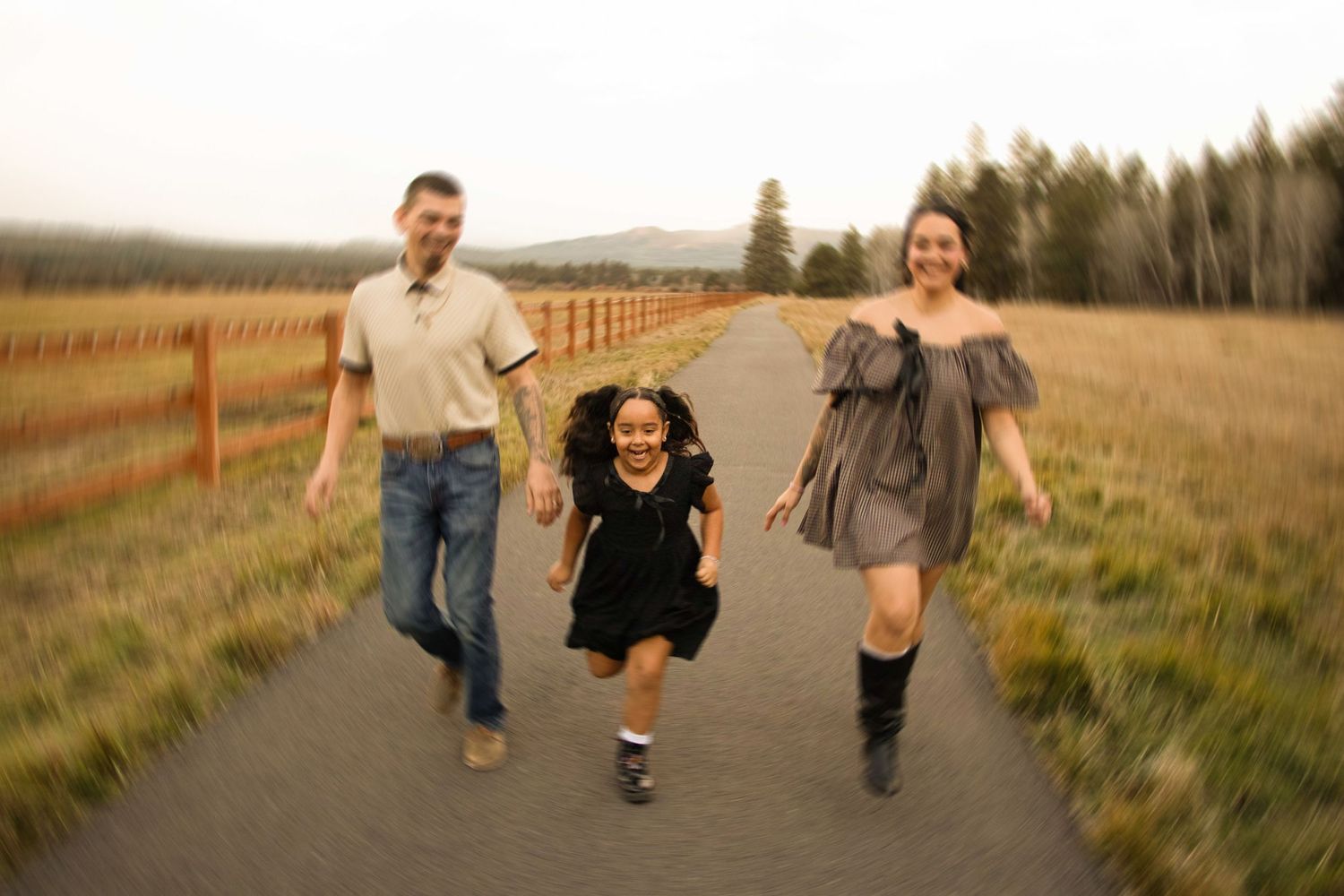 a mom and dad run with their young daughter down a paved path in Sisters, Oregon, with a horse pasture beside them