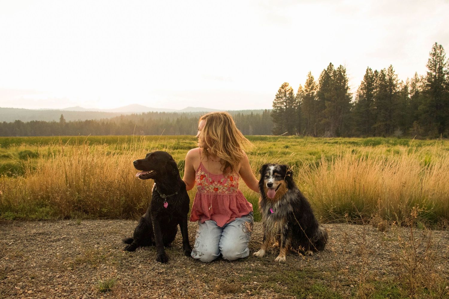 a young woman sits with her two dogs in a field at Dillon Falls in Central Oregon