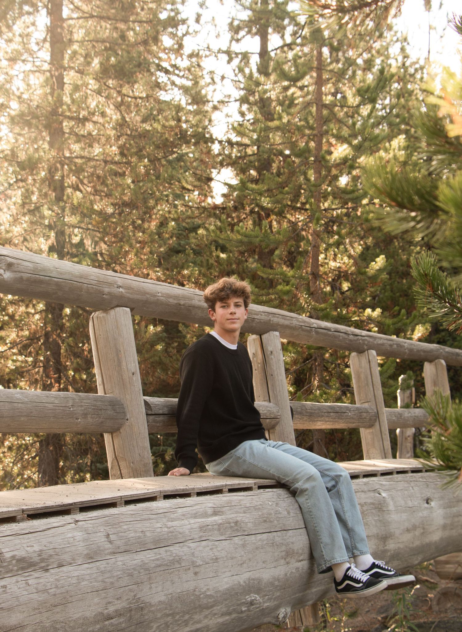 a high school senior sits on a log bridge over the Deschutes River