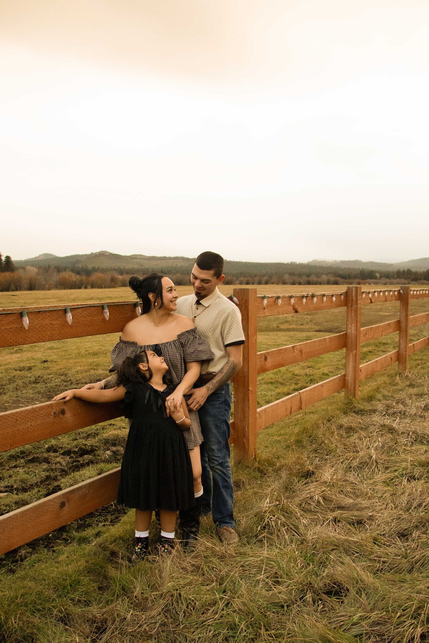a mom and dad lean against a rustic wood fence in Sisters, Oregon, with a horse pasture beside them