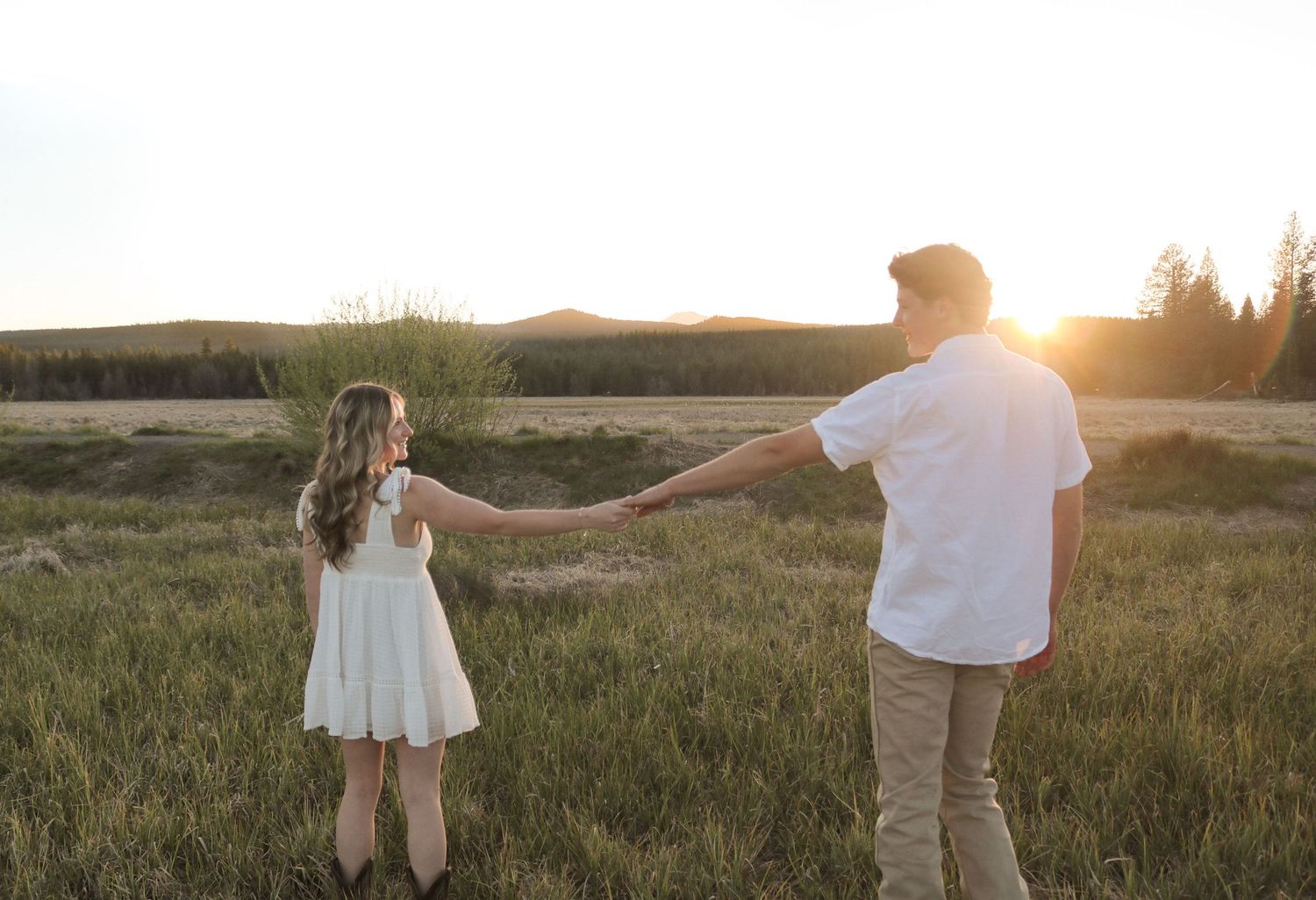 a couple holds hands in a sunlit, Bend, Oregon field