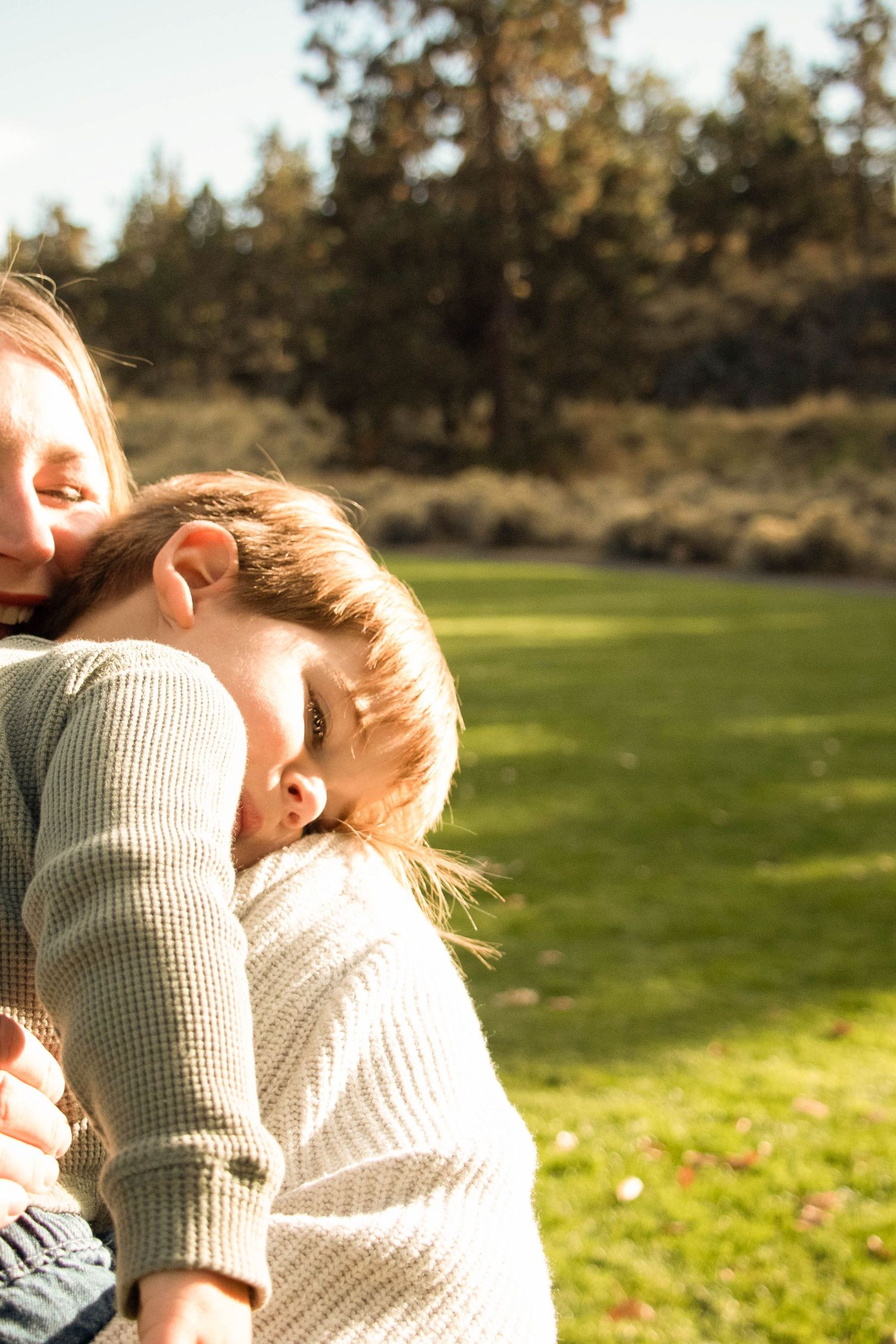 a toddler boy lays his head on his mom's shoulder at a park in Bend, Oregon