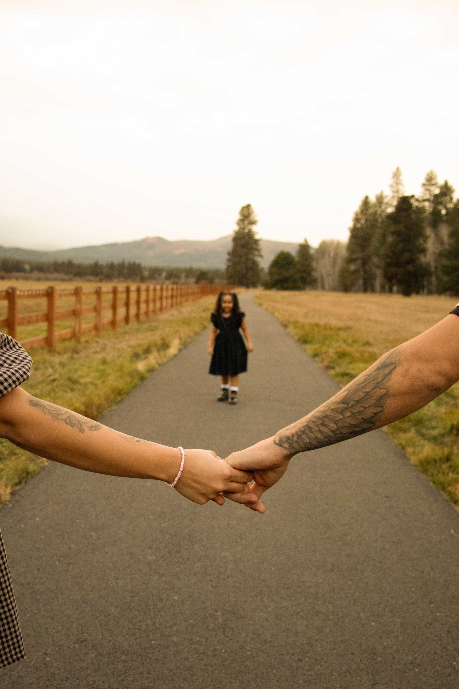 a daughter runs down a paved path in Sisters, Oregon, with a horse pasture beside her, with her parents holding hands in front of her