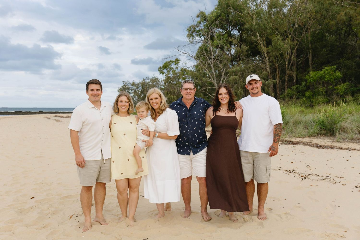 Family group wearing coordinated neutral colors poses on sandy beach.