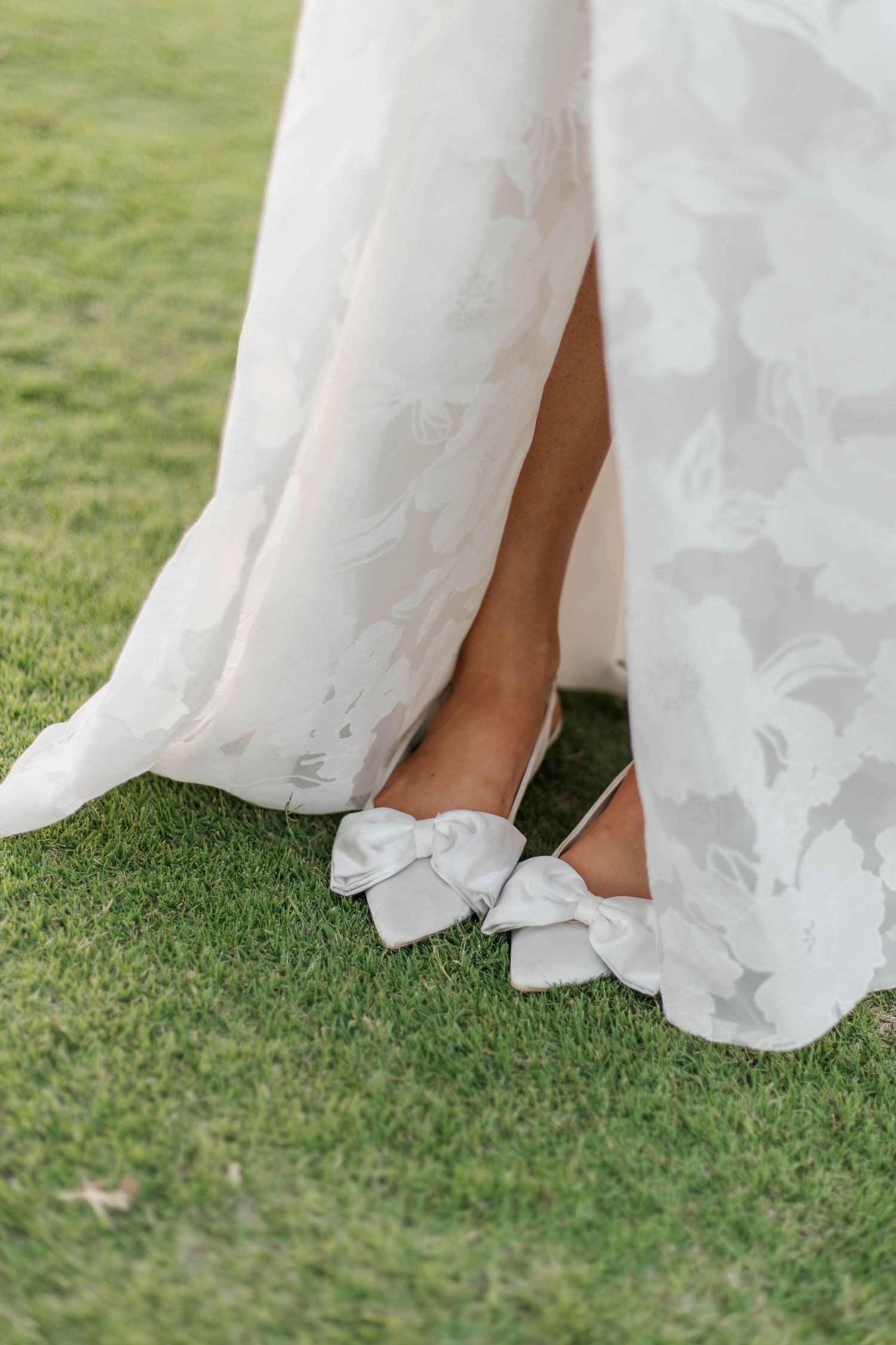 Close-up of white wedding dress and shoes on green grass during outdoor ceremony.